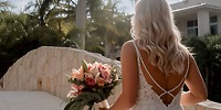 Bride in lace dress at destination wedding, Generations Riviera Maya, holding rose bouquet by stone steps.