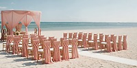 Pink draped chairs arranged for a destination wedding on the sandy oceanfront at Generations Riviera Maya.