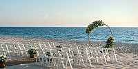 A beach wedding setup at the Grand Palladium Kantenah featuring white chairs arranged in rows and a circular floral arch overlooking the ocean.