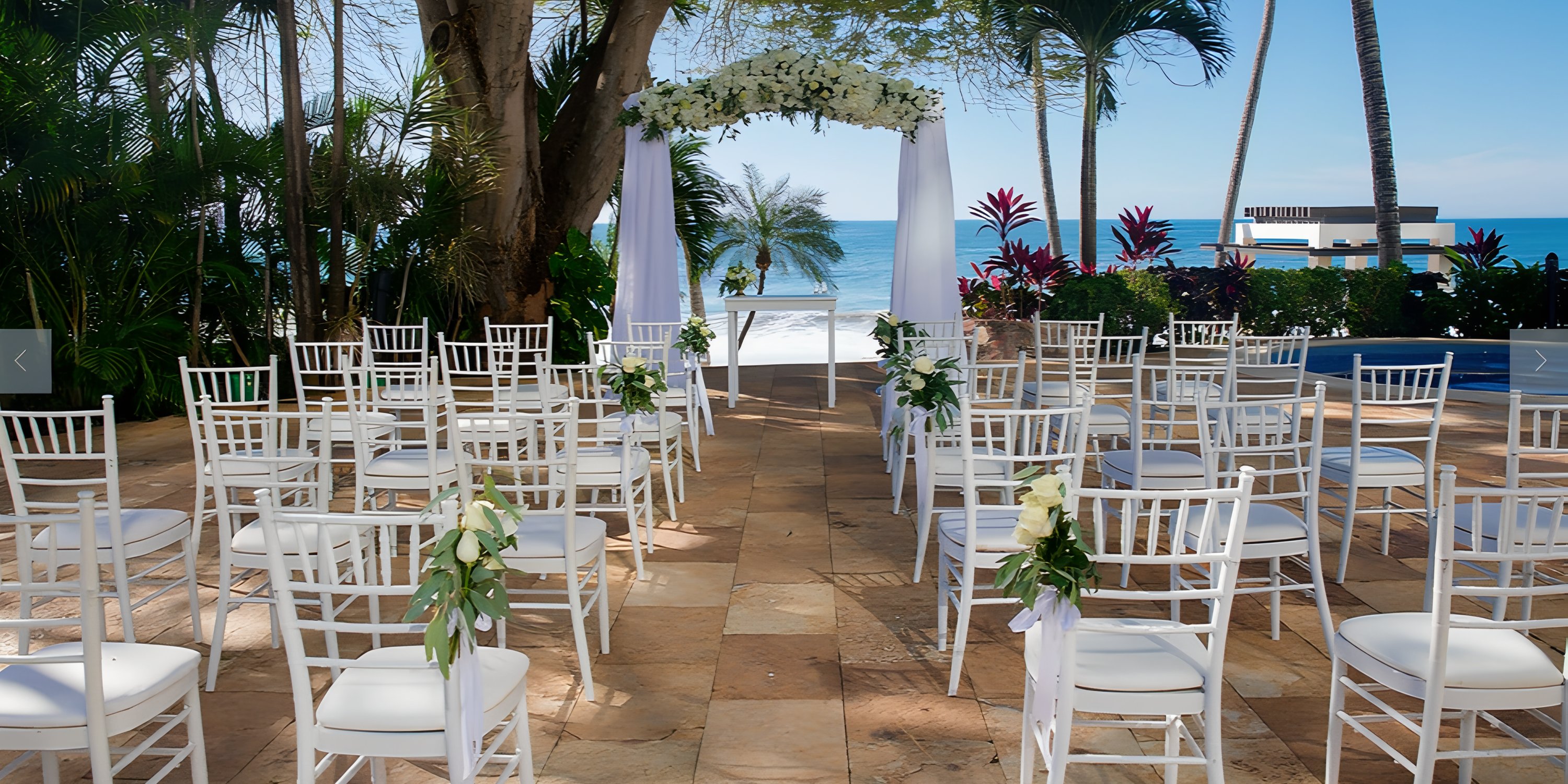 Destination wedding setup at Hyatt Ziva Puerto Vallarta with white chairs and floral arch by the ocean.
