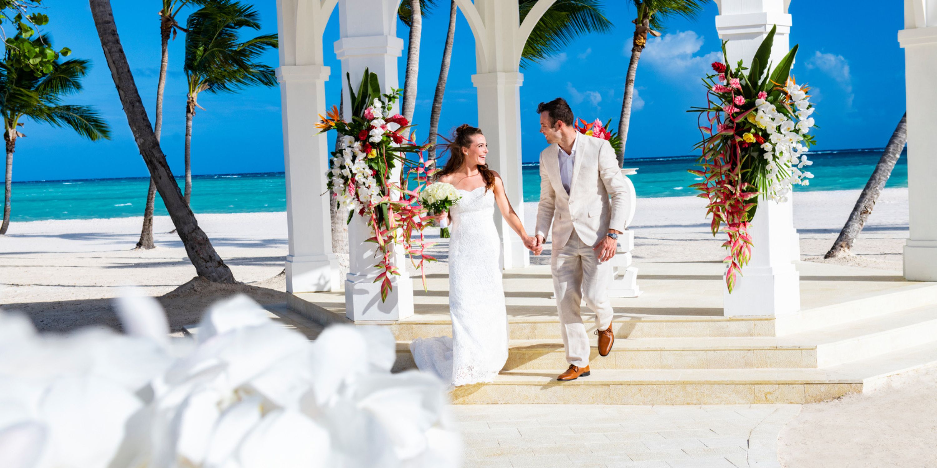 At the Hyatt Ziva Cap Cana, the bride and groom hold hands during their tropical destination wedding on the beach.