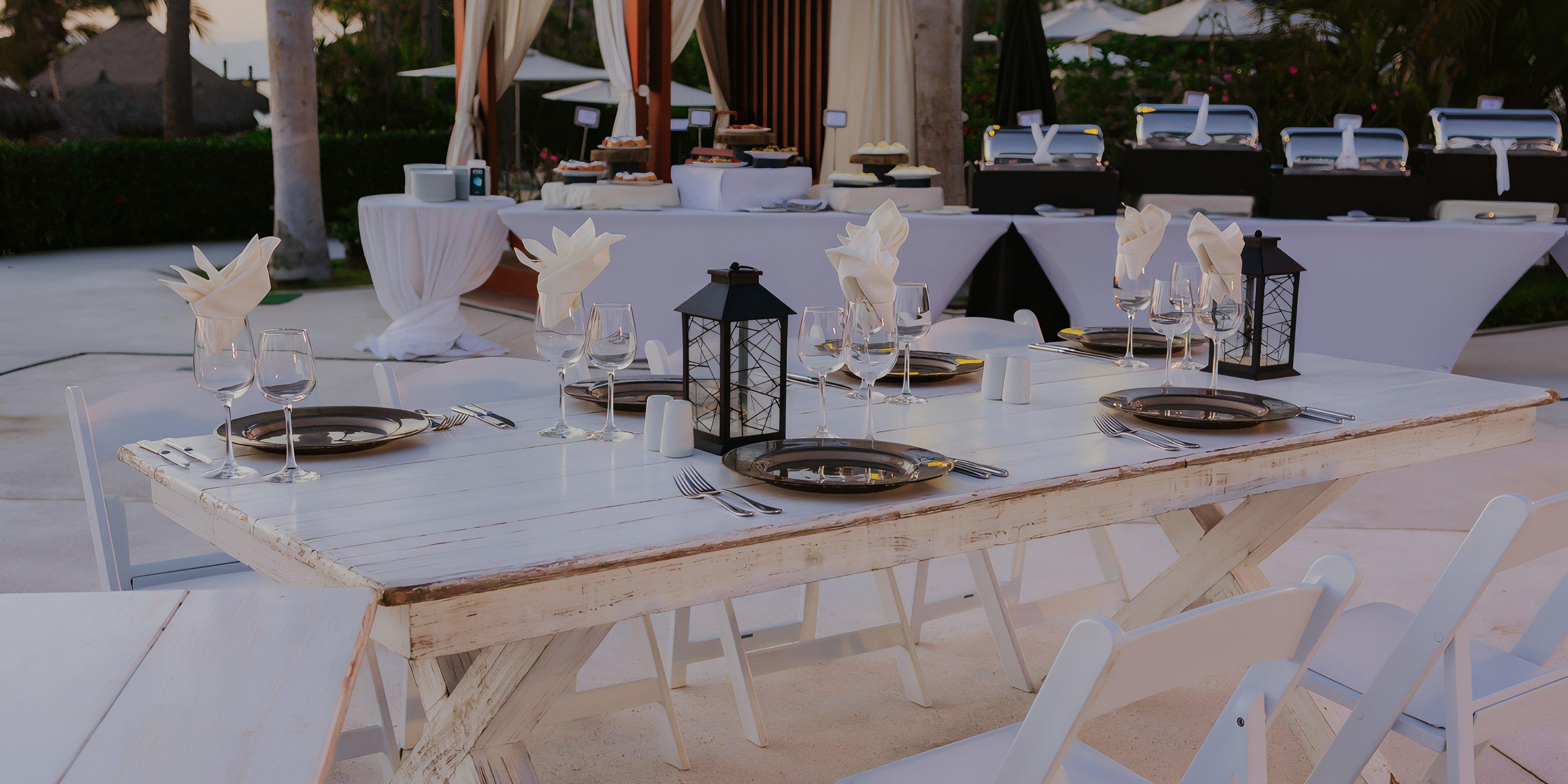 Destination wedding setup at Hard Rock Vallarta: white table for six with black lanterns, plates, napkins.