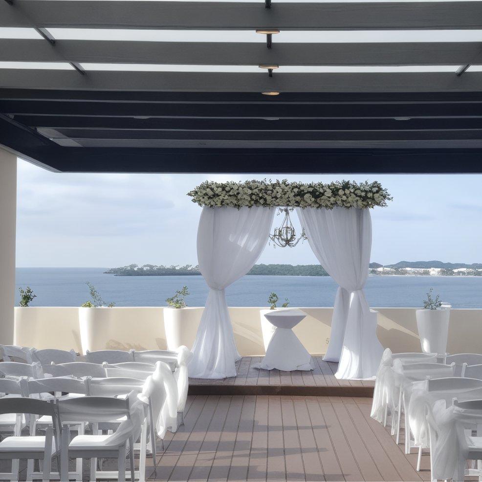 Destination wedding ceremony arrangement featuring white chairs and a floral arch facing the ocean.