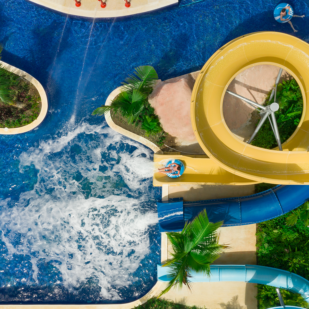 Aerial view of Hilton La Romana featuring people on colorful slides splashing into a pool surrounded by palm trees.
