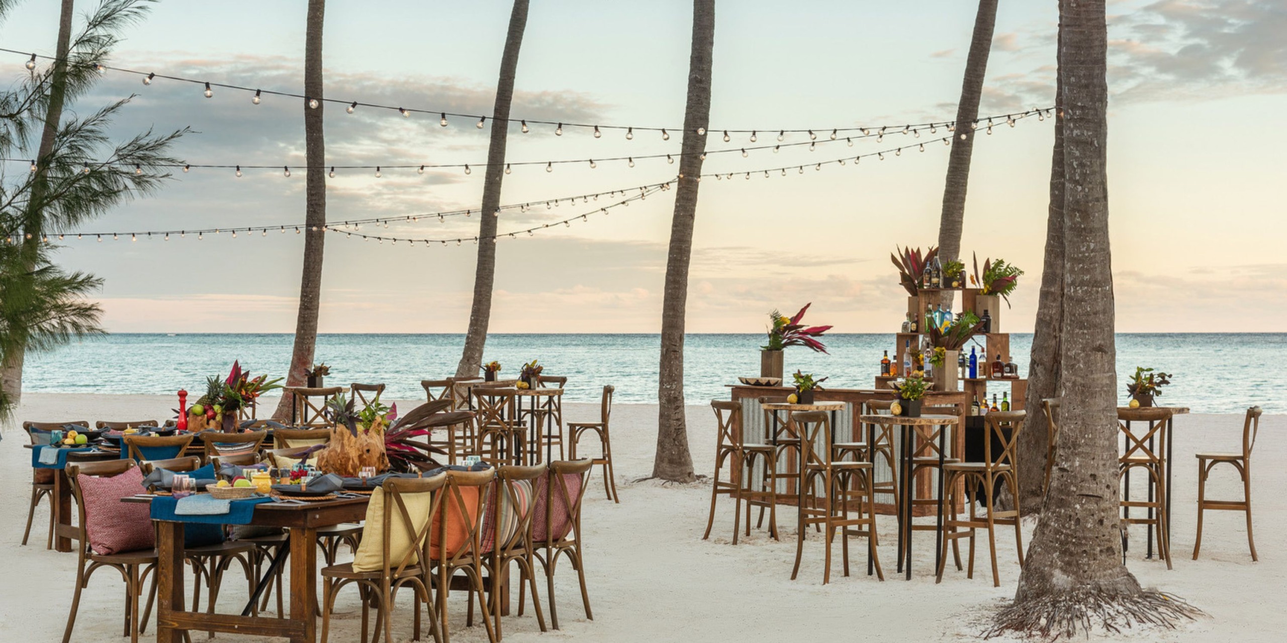 Sunset at Hyatt Zilara Cap Cana is the perfect setting for a destination wedding, with wooden tables, elegant chairs, and string lights adorning the beach.