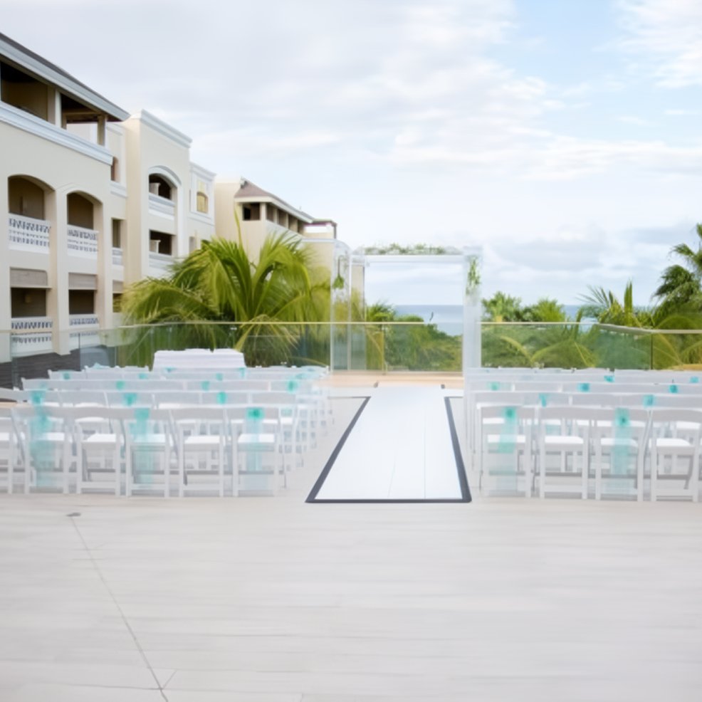 White chairs arranged in rows on a terrace by palm trees, ready for a destination wedding ceremony.