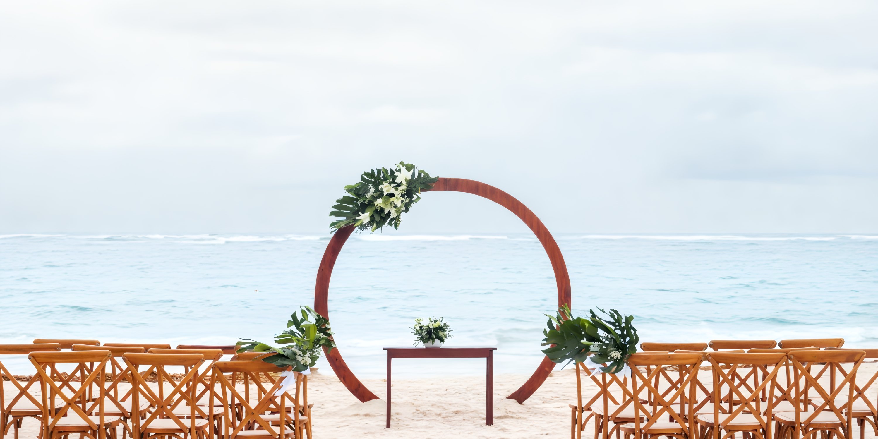 Wooden chairs face a greenery arch set up for a destination wedding on the beach at Iberostar Waves Punta Cana.
