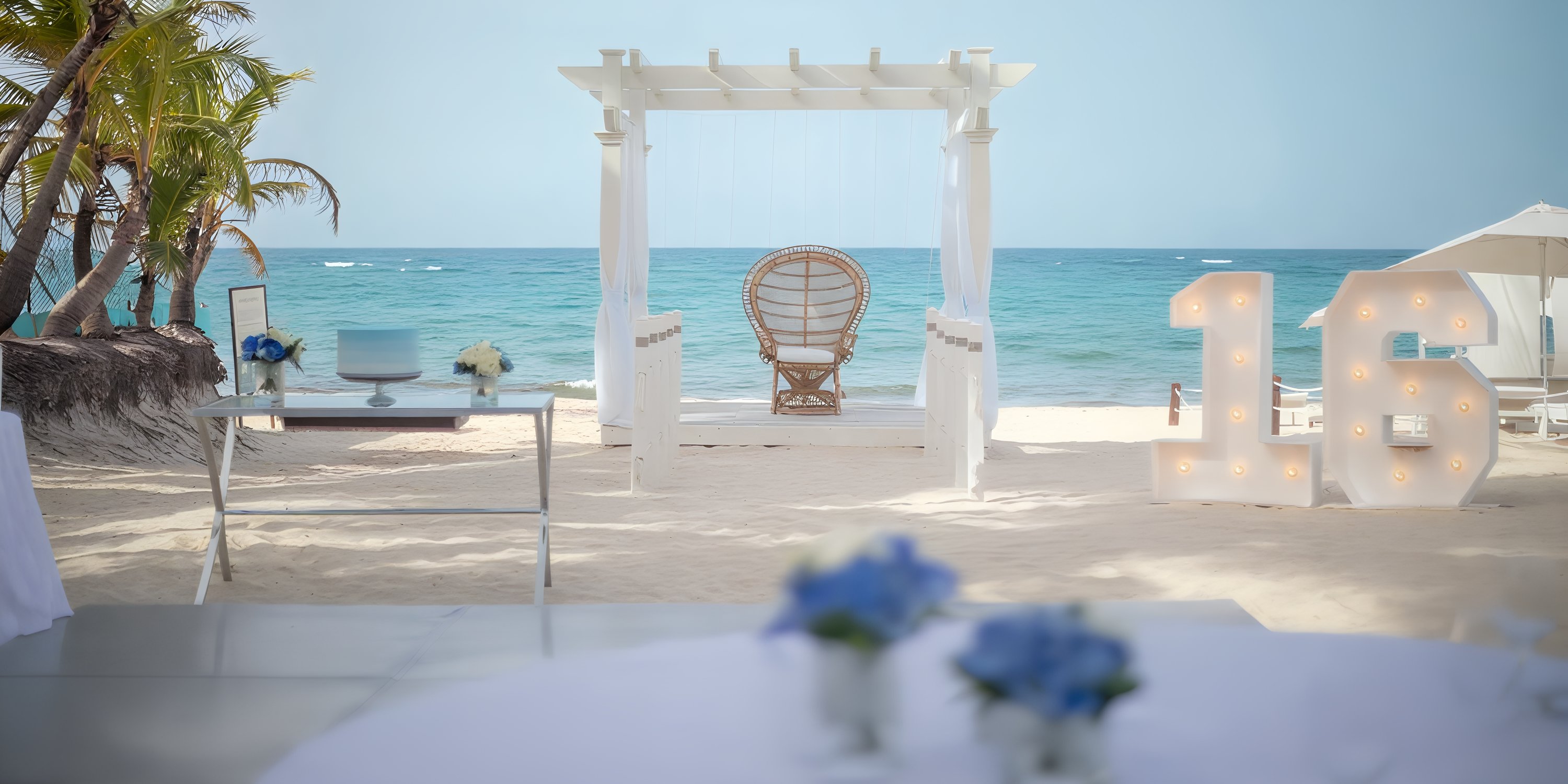 Destination wedding setup at Iberostar Waves Punta Cana featuring a white pergola, wicker chair, and "16".