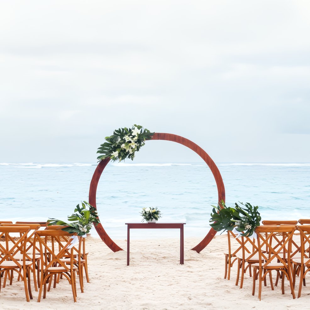 Destination wedding scene featuring wooden chairs, a floral arch, and a table overlooking the ocean.