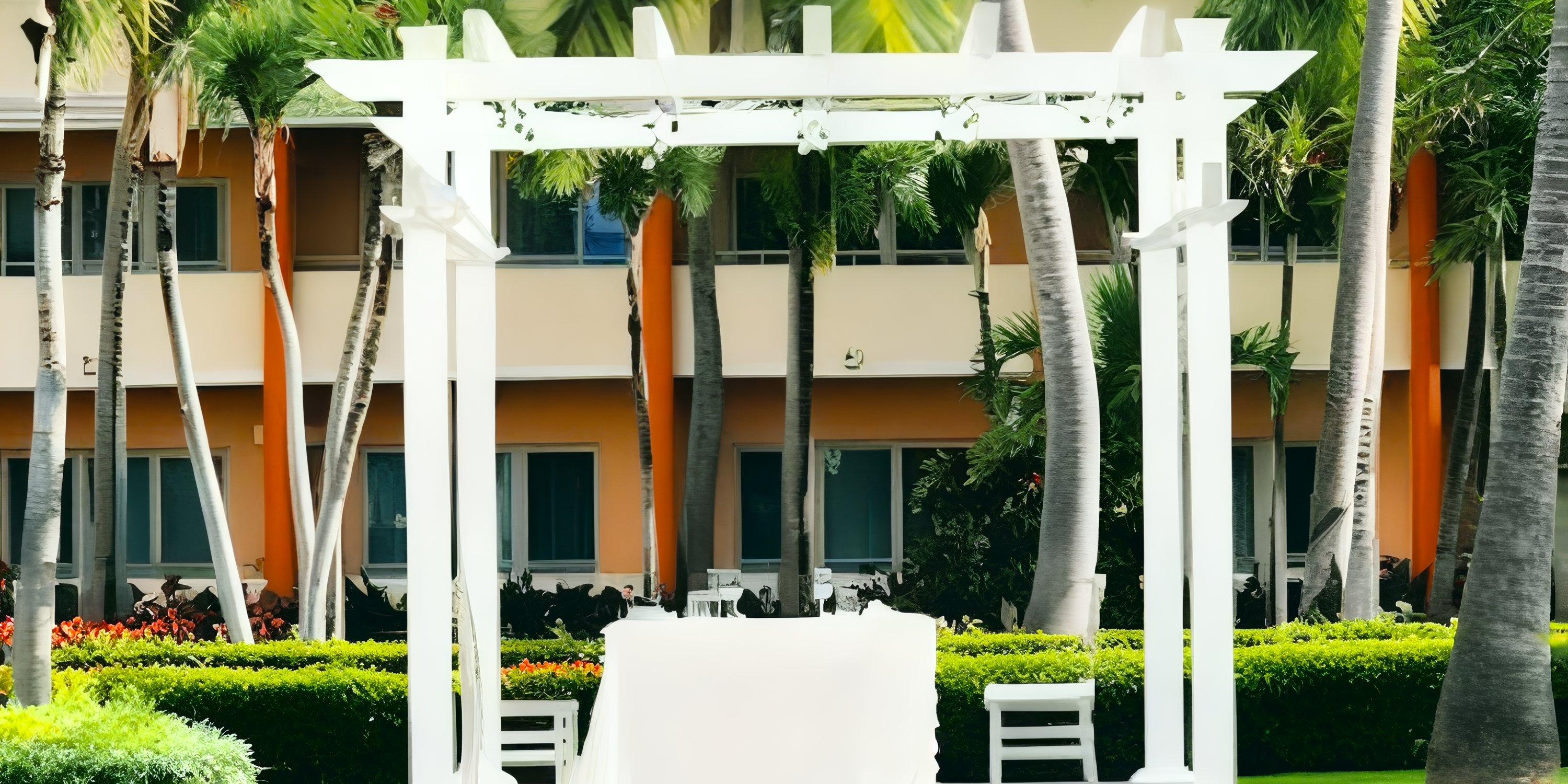 Destination wedding setup at Iberostar Waves Punta Cana with arbor, chairs, palm trees, and nearby building.