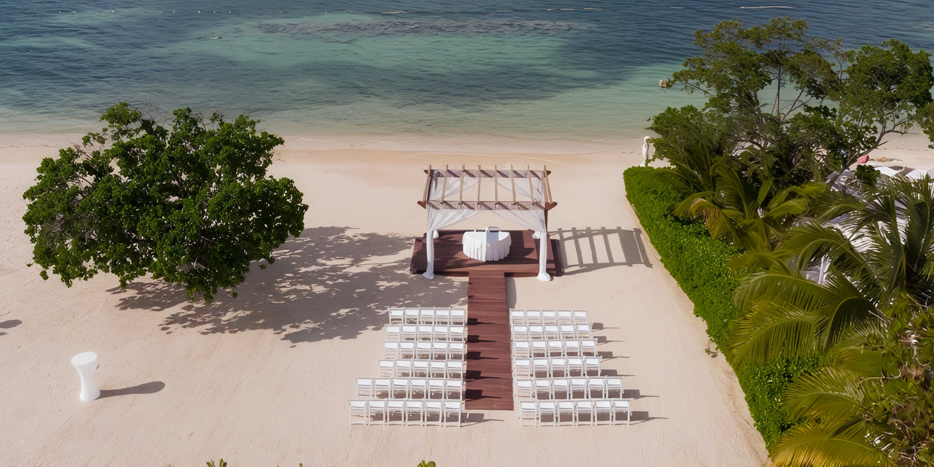 A destination wedding at Iberostar Selection Rose Hall Suites, white chairs facing an oceanfront altar.