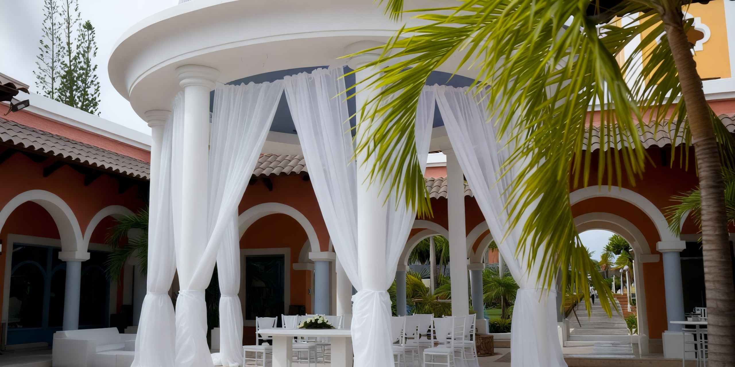 White columns, palm leaves, and arches create a picturesque setting for a destination wedding at the Iberostar Waves Dominicana courtyard.