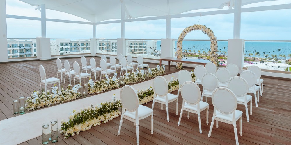 Experience your dream destination wedding at Planet Hollywood Cancun, featuring a stunning outdoor venue with white chairs, beautiful floral arrangements, and breathtaking ocean views.