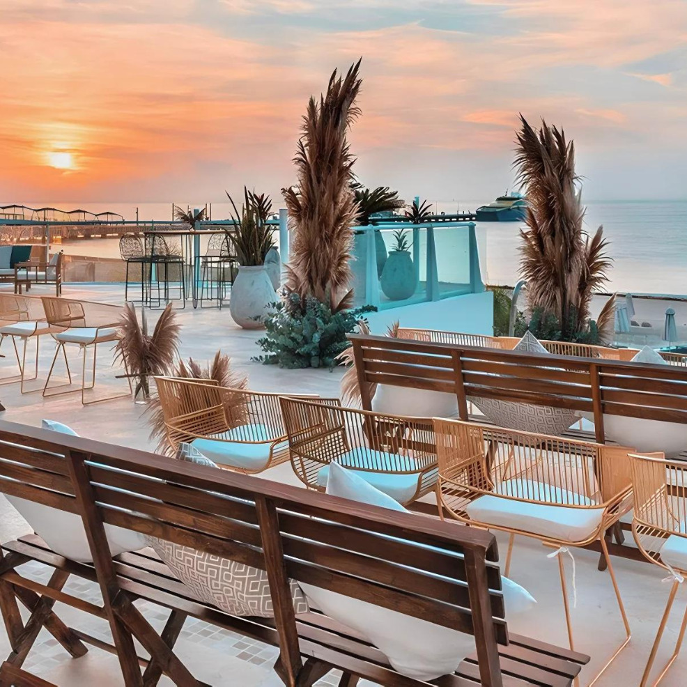 Sunset view from a stylish rooftop terrace designed for a destination wedding, with seating arrangements, glass barriers, and tropical plants overlooking the ocean.