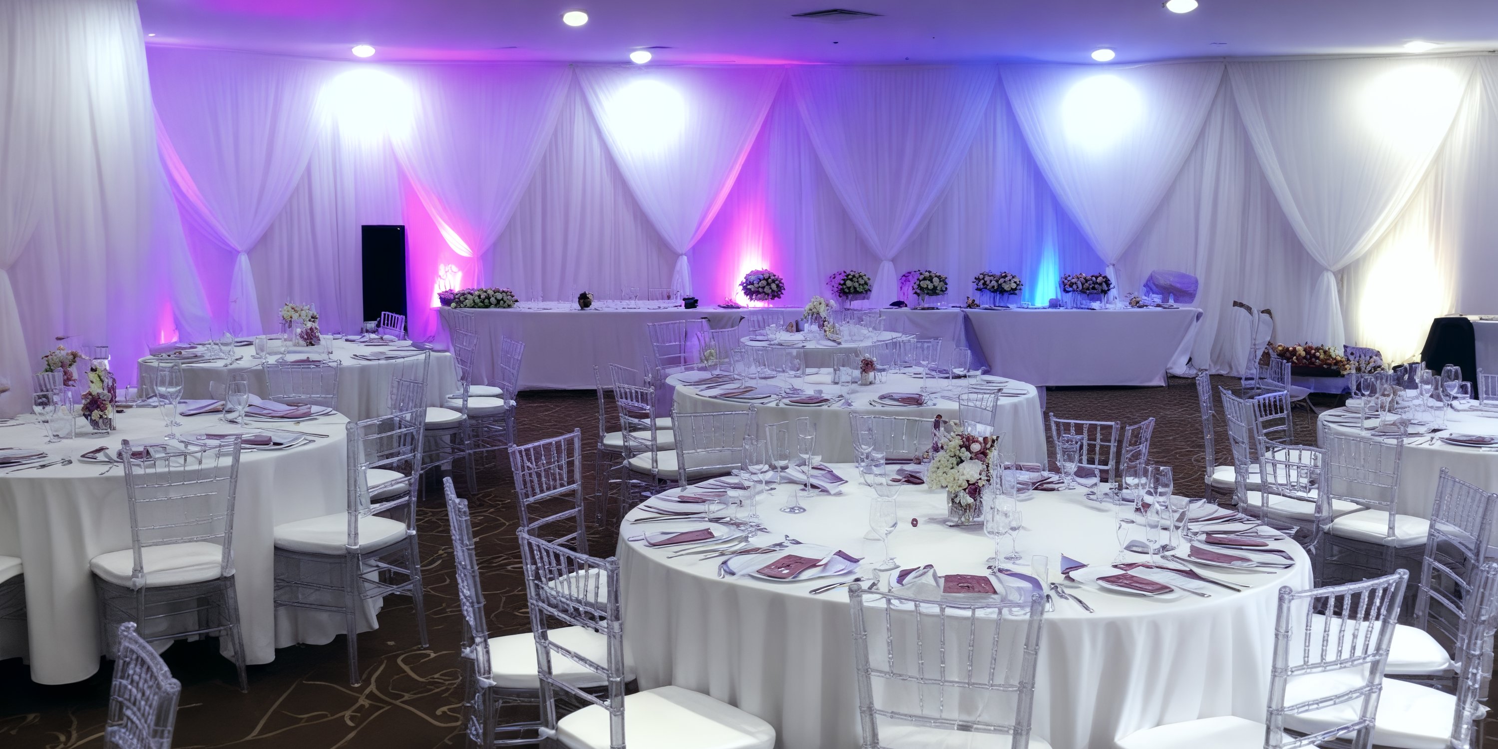 Wedding banquet hall at Royalton Blue Waters with round tables, white linens, and purple lighting.