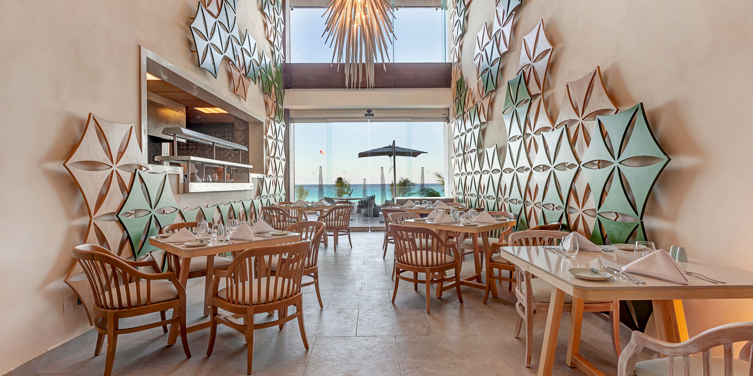 Chic destination wedding restaurant at Royalton CHIC Suites Cancun with geometric decor, wood chairs, ocean views.