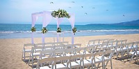 White chairs and a floral arch set up for a destination wedding on the beach at Hotel Riu Jalisco.