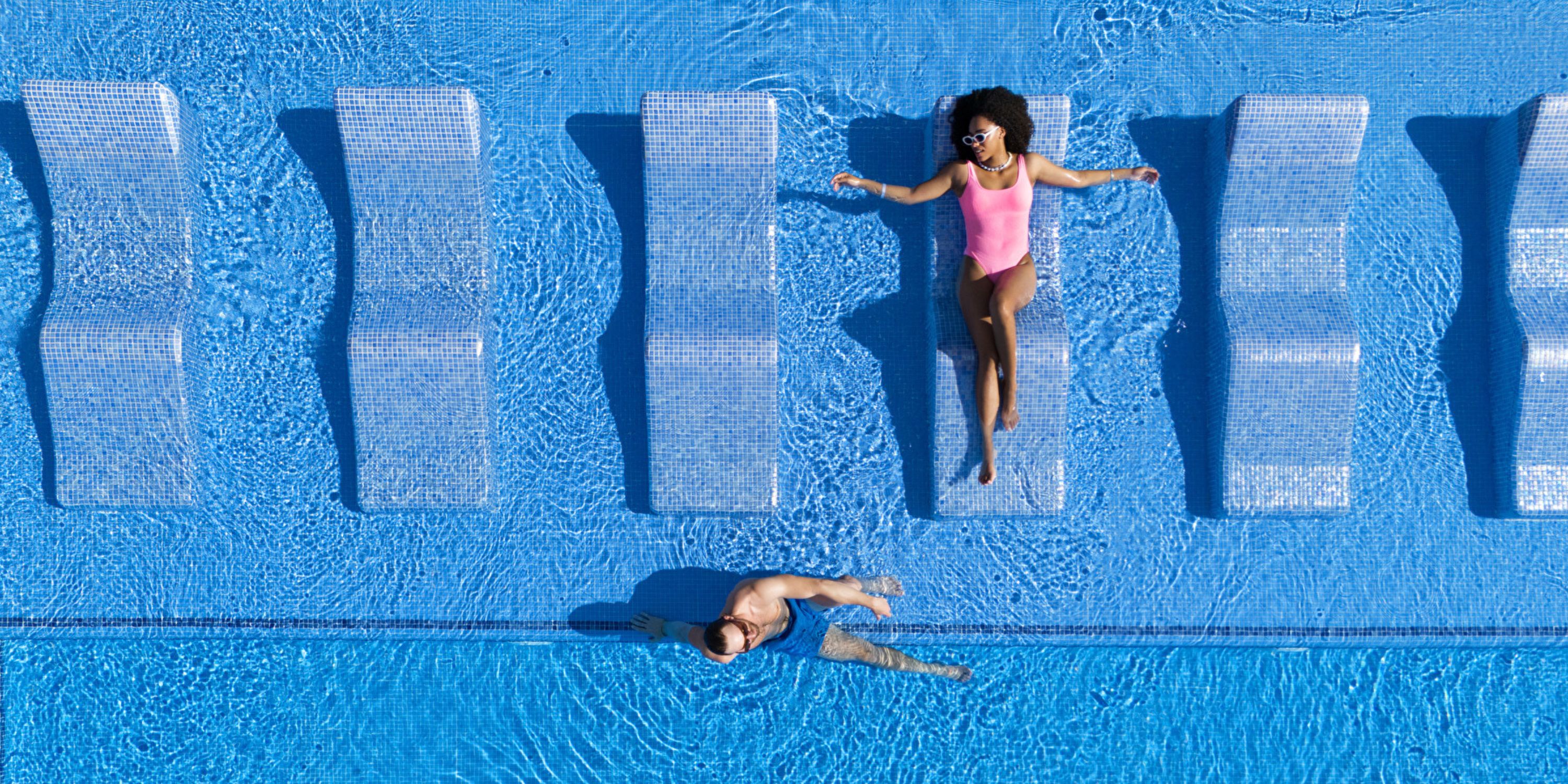 At a destination wedding, two guests relax at Hotel Riu Jalisco’s pool—one lounging, one swimming.