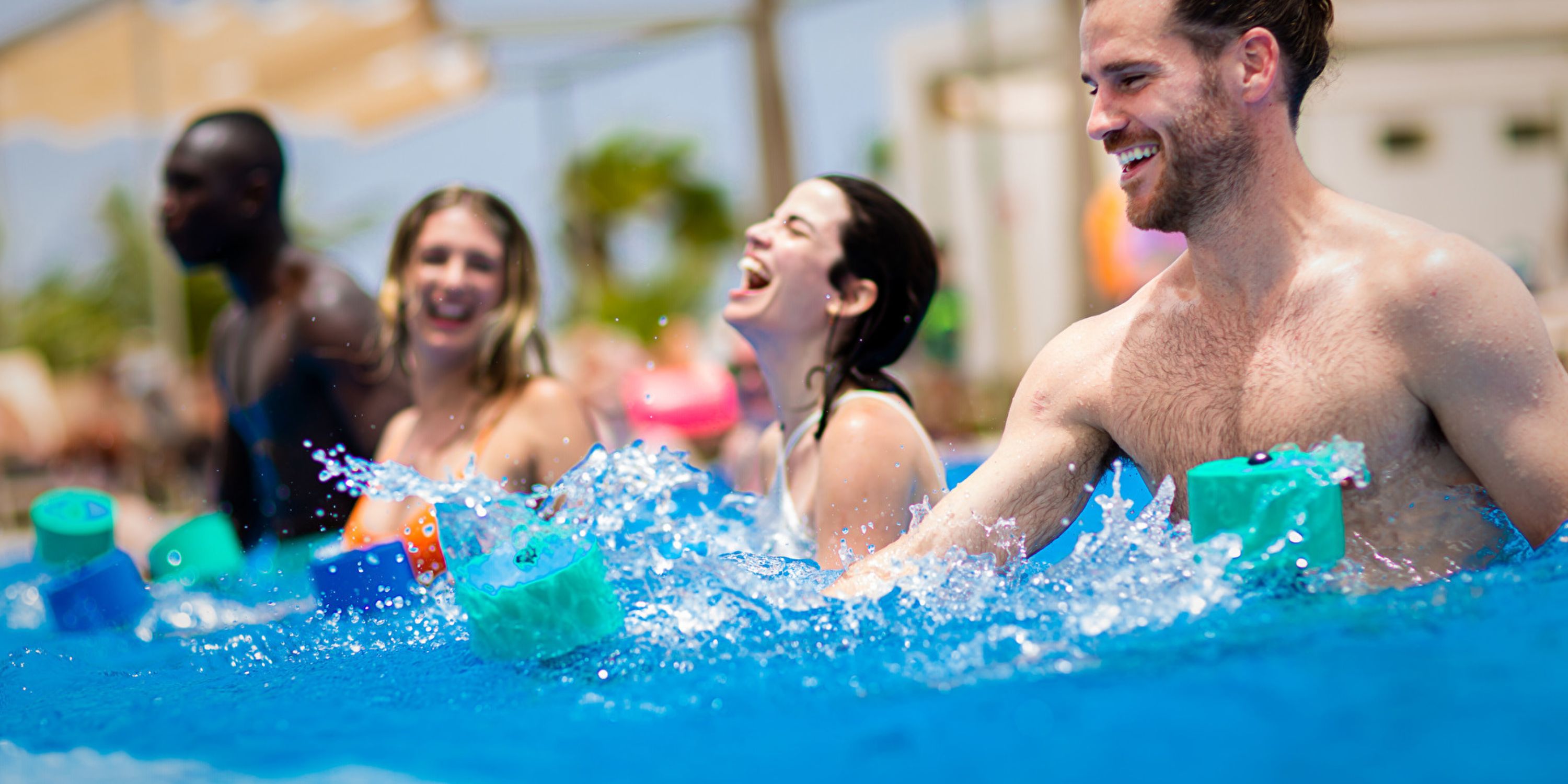 Four adults at a destination wedding have fun with foam toys in the pool at Hotel Riu Jalisco.