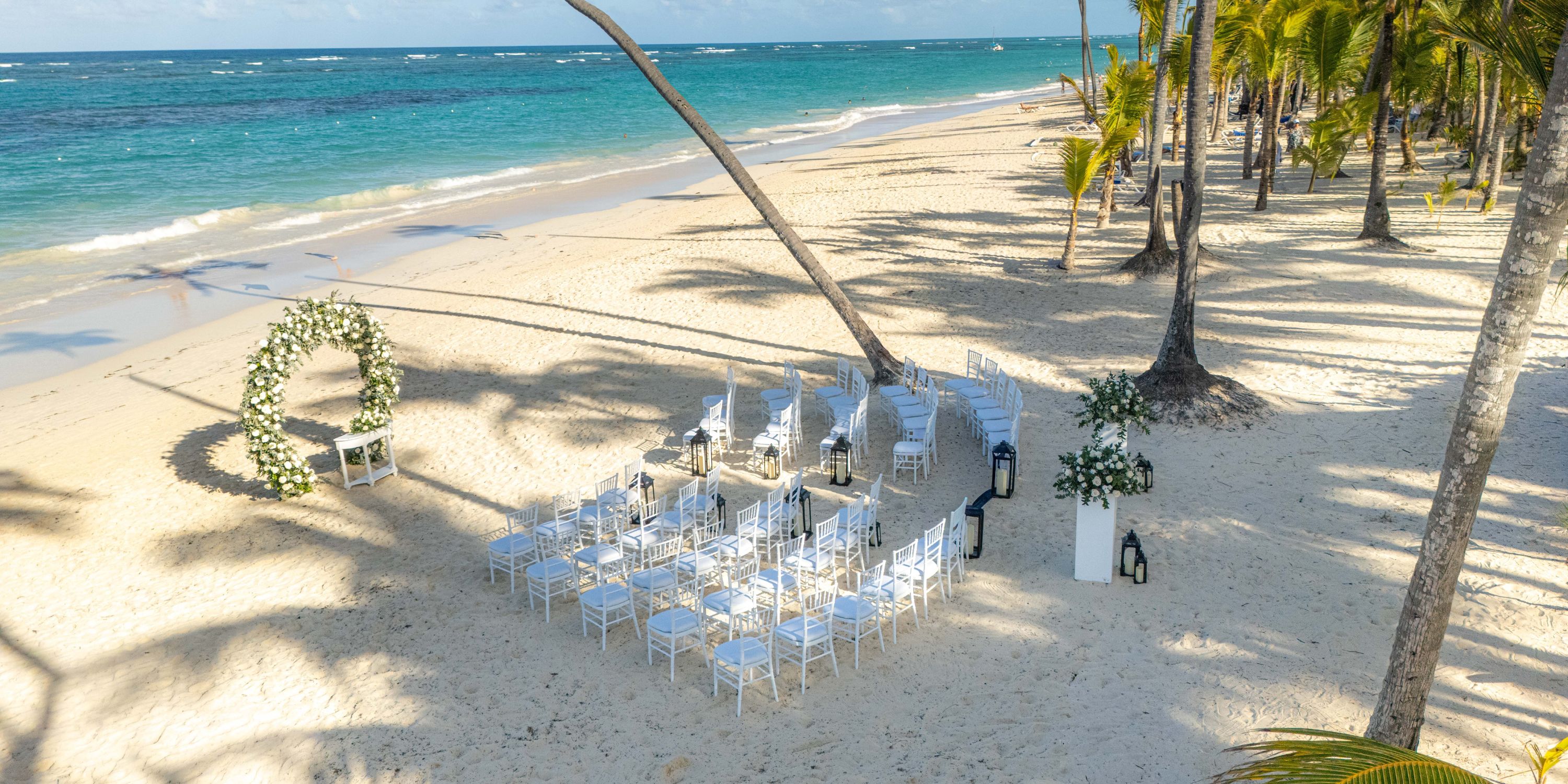 White chairs and floral arch arranged for a destination wedding ceremony at Hotel Riu Bambu beach.