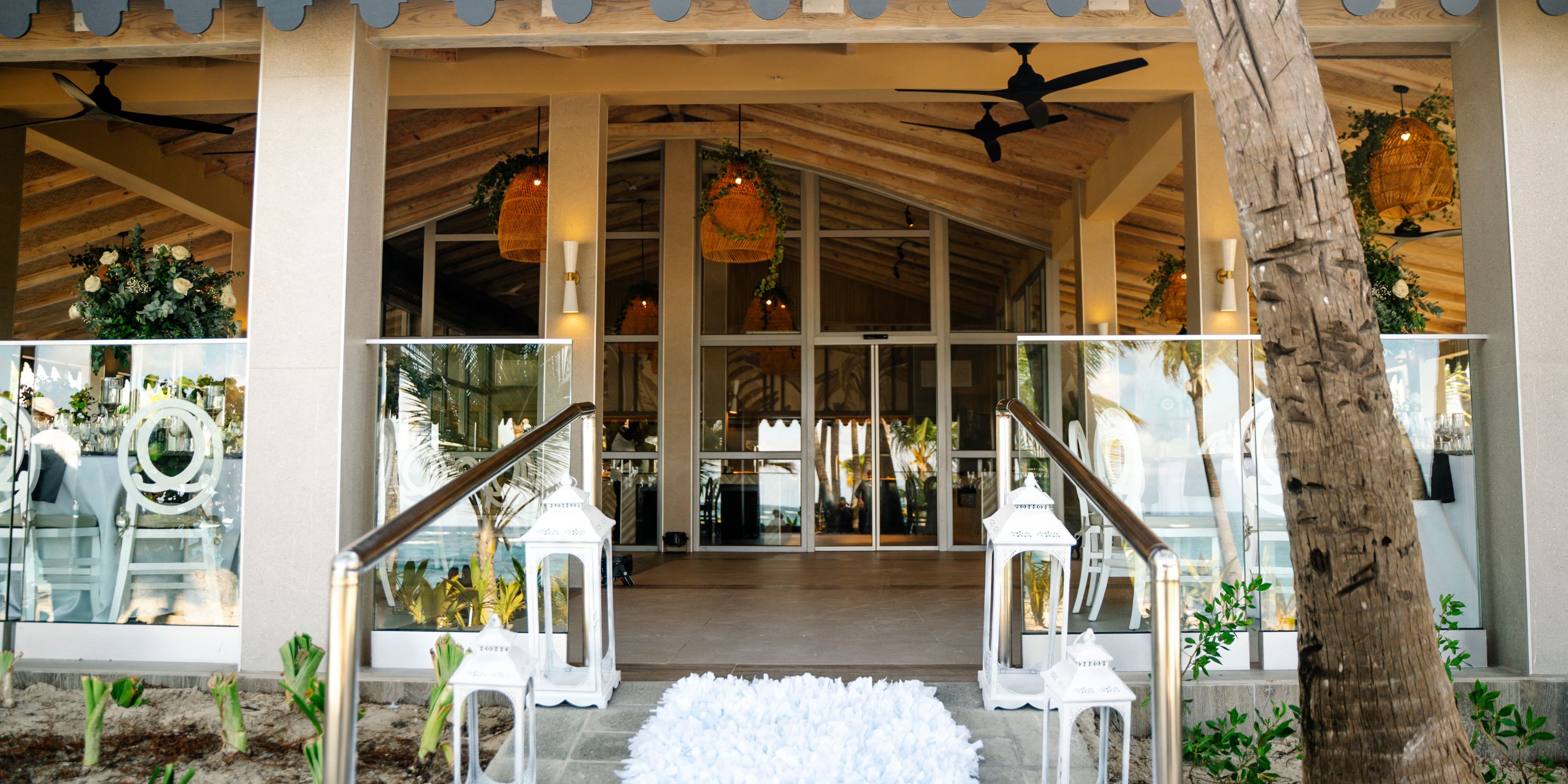 Entrance to Hotel Riu Bambu&rsquo;s open-air wedding venue with glass doors, white chairs, and hanging lights.