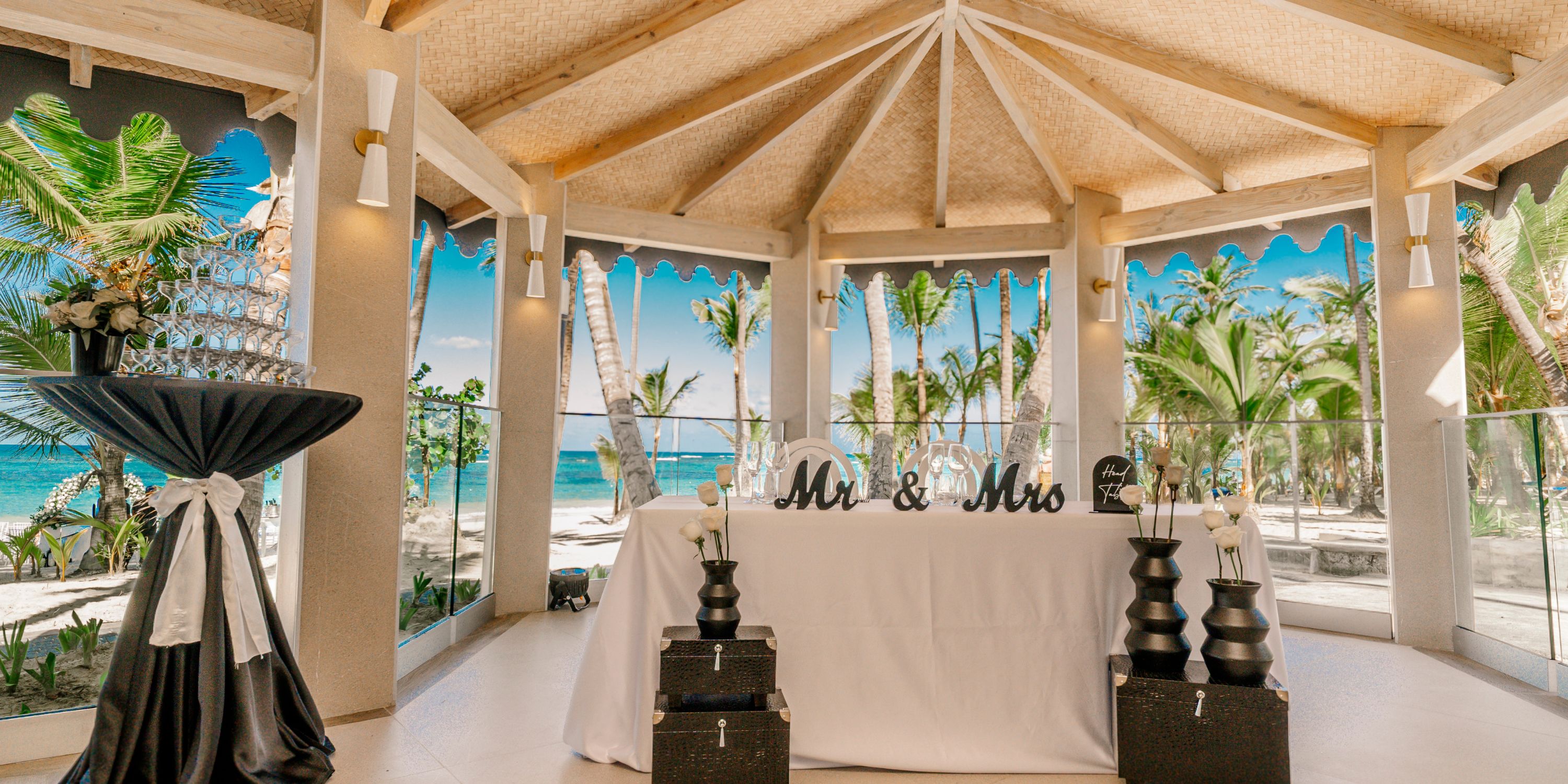 Destination wedding setup at Hotel Riu Bambu, featuring a "Mr & Mrs" sign and palm trees outdoors.