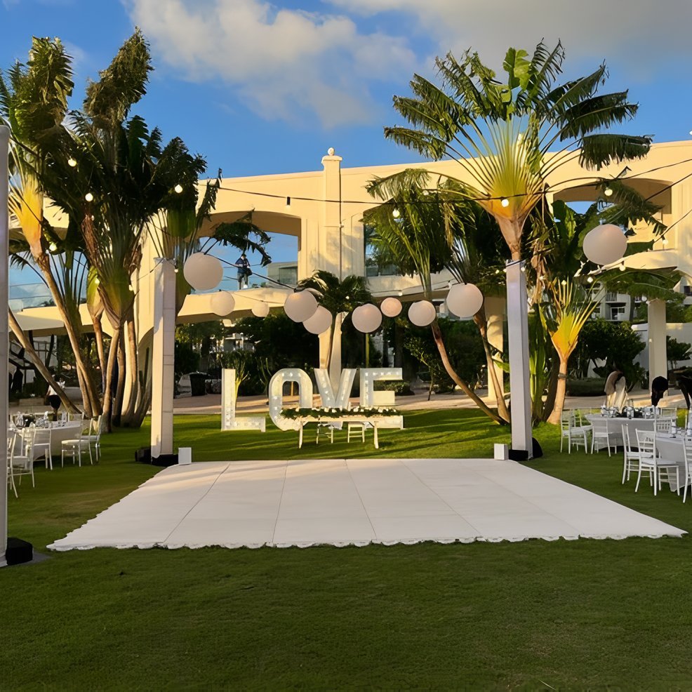 Destination wedding setting featuring white decor, round tables, and giant "LOVE" letters on the lawn.