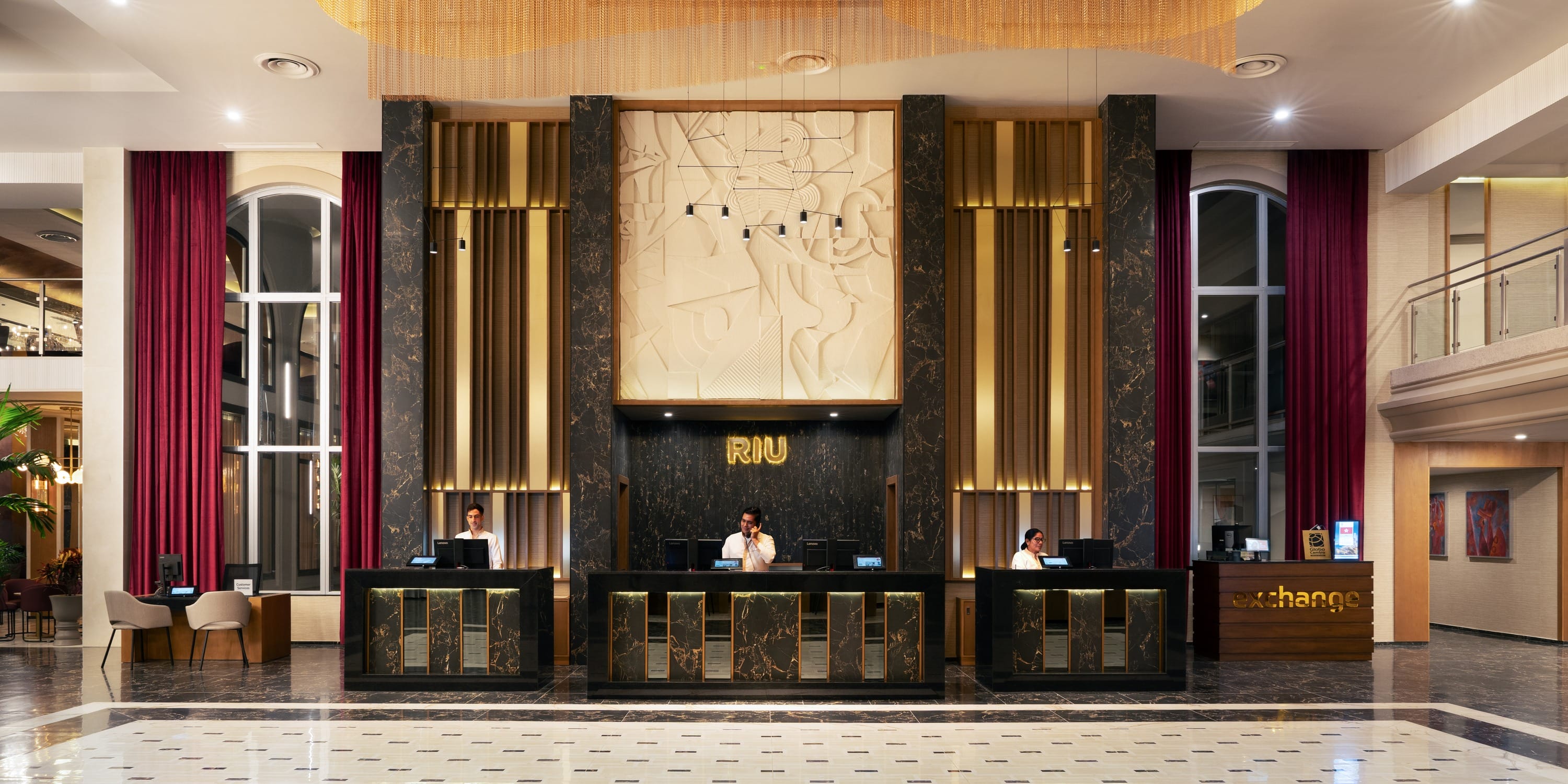 Three staff members at the Hotel Riu Palace Mexico destination wedding reception desk in a lobby.