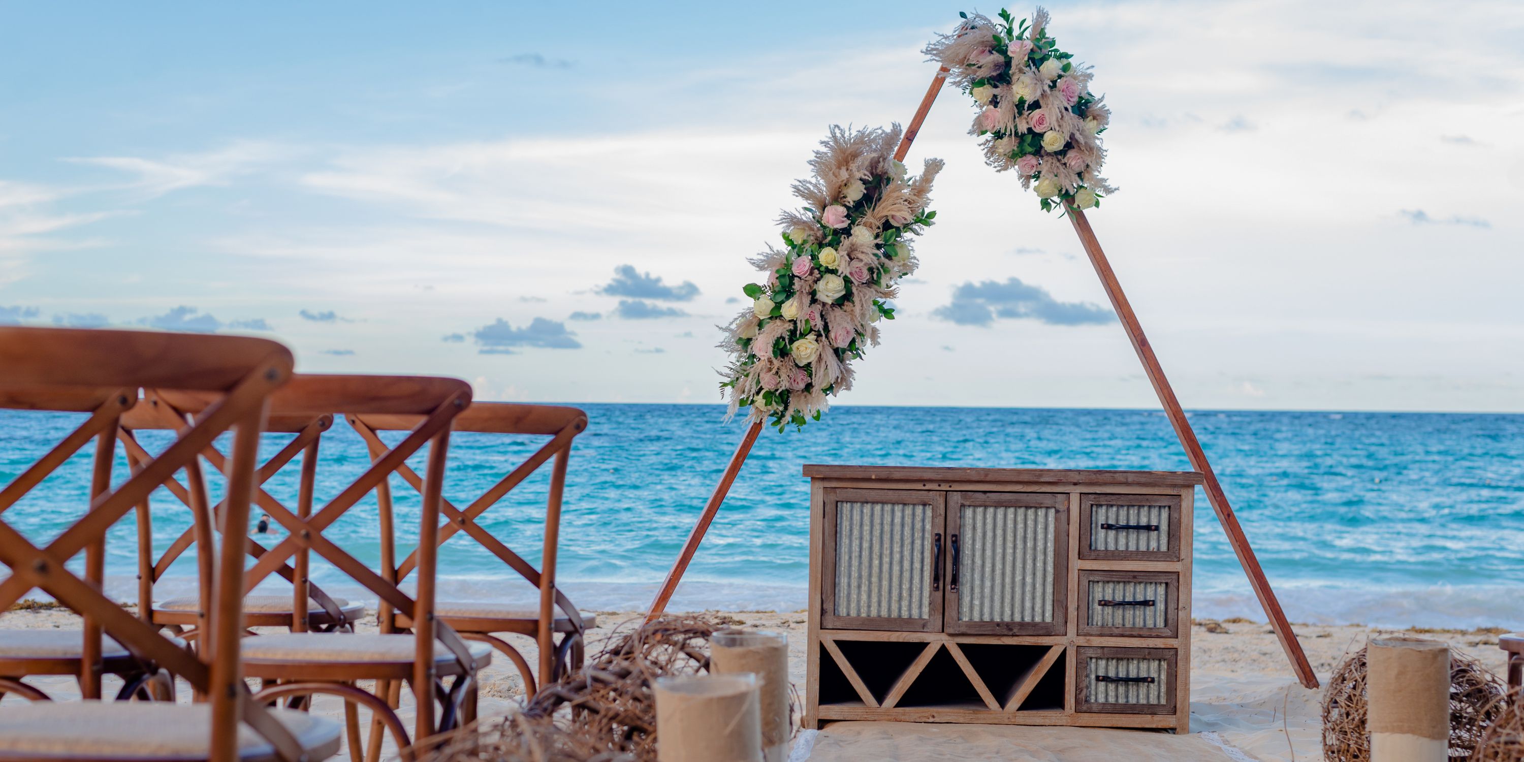 Destination wedding ceremony at Hotel Riu Palace Punta Cana with wooden chairs and a triangle arch.
