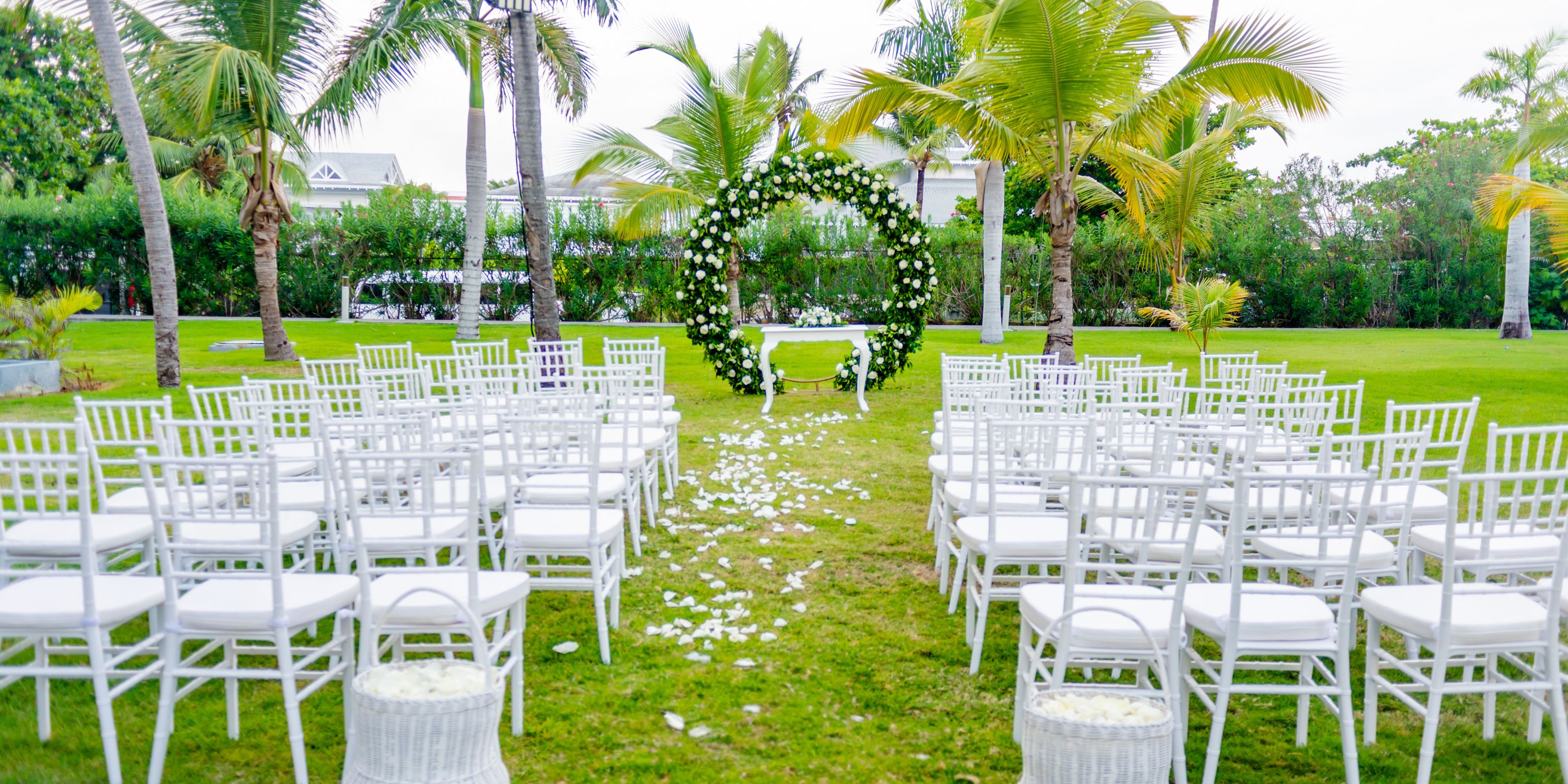 Destination wedding ceremony at Hotel Riu Palace Punta Cana with white chairs, petals, and a floral arch.