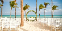 White chairs and a beautiful floral arch arranged for a destination wedding on the beach at Hotel Riu Palace Riviera Maya.
