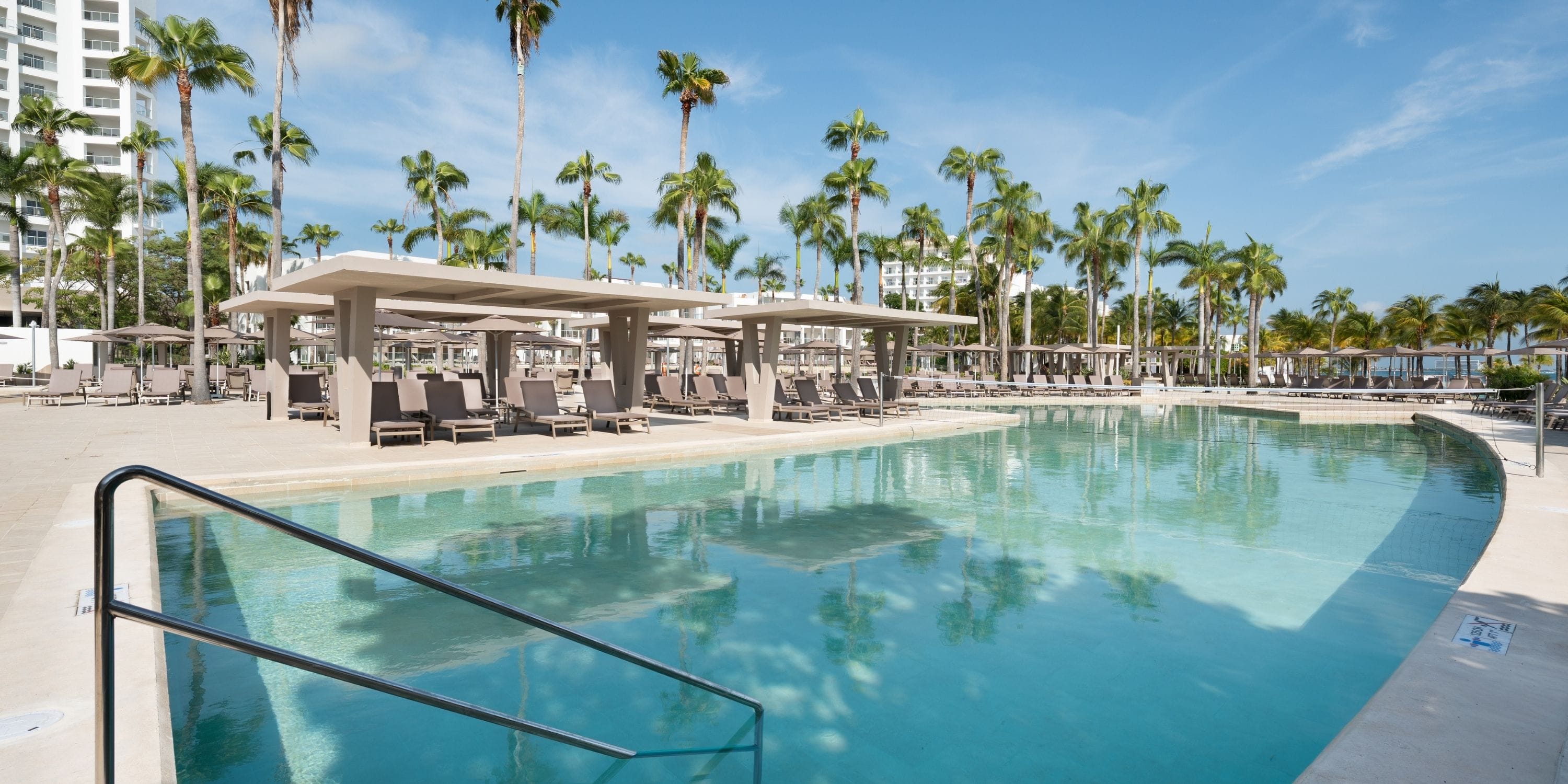 Hotel Riu Palace Peninsula&rsquo;s pool, perfect for weddings, with lounge chairs and palm trees.