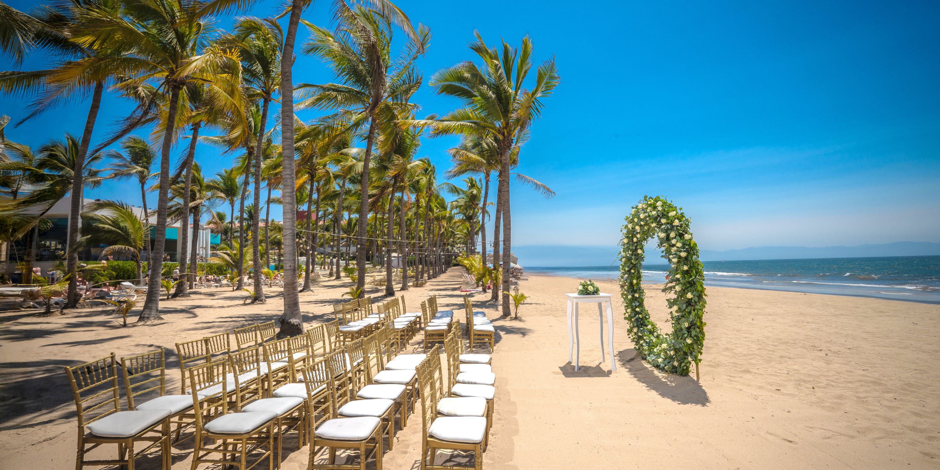 Rows of chairs face a floral arch on the sand, prepared for a destination wedding at Hotel Riu Vallarta.