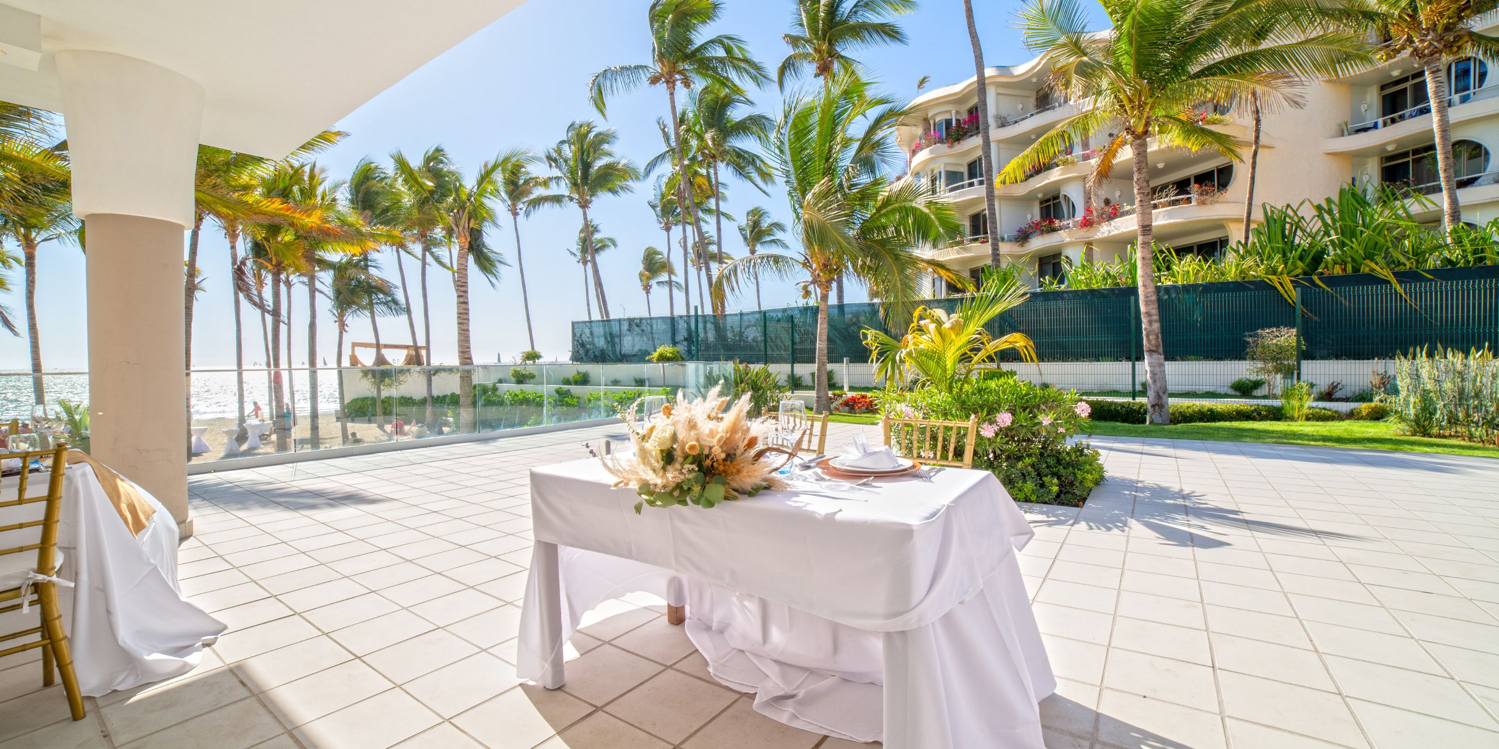 White table for two on the sunny patio of Hotel Riu Vallarta, perfect for a destination wedding, with palm trees.