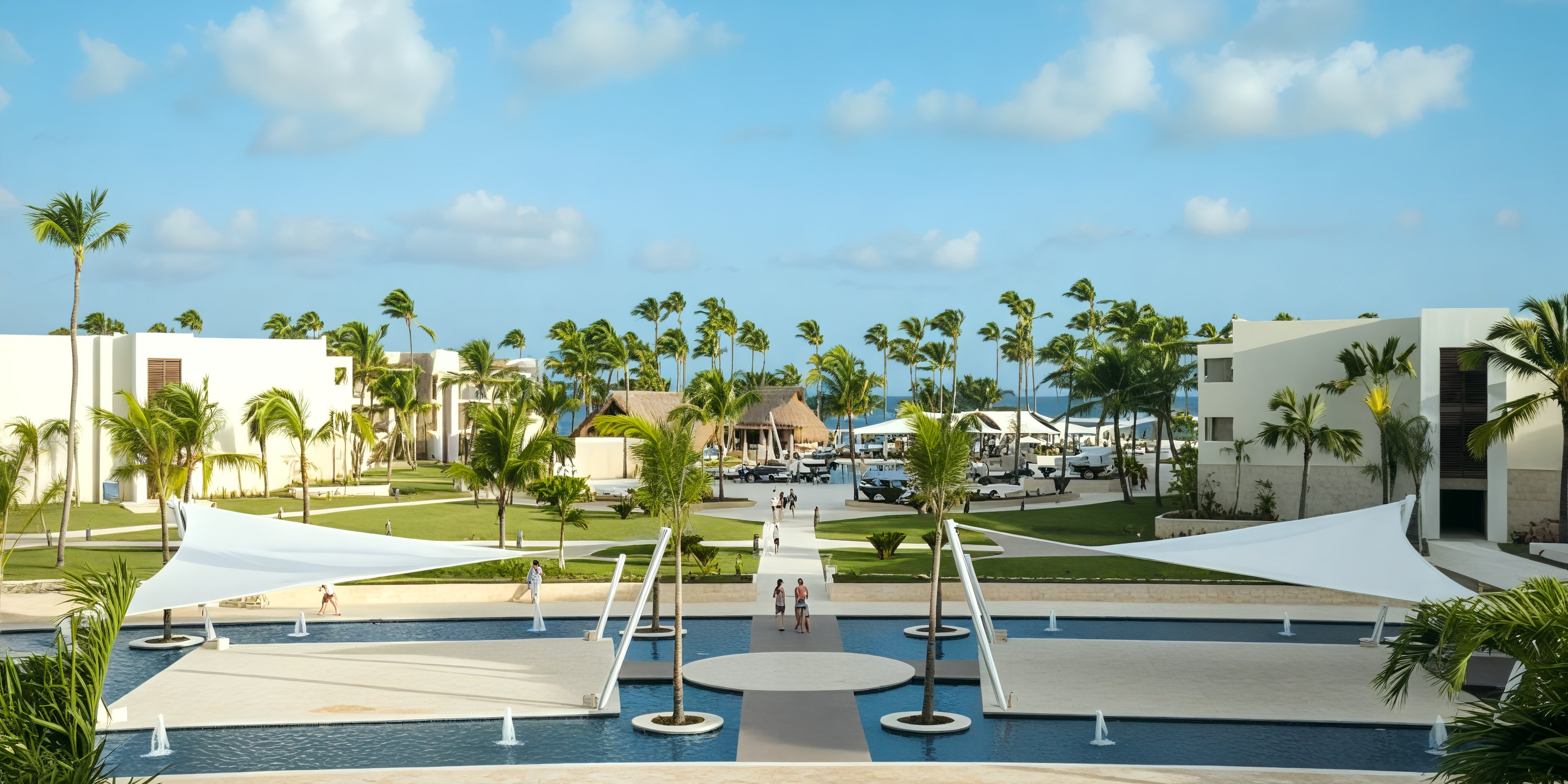 Royalton Punta Cana: a picturesque poolside resort, adorned with palm trees and sleek modern buildings beneath a clear blue sky, perfect for an unforgettable destination wedding.