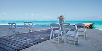 White chairs set for a destination wedding at Hotel Riu Cancun, with a wooden walkway and pier nearby.