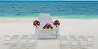 Elegant white chairs and floral decor set up for a destination wedding by the ocean at Hotel Riu Cancun.