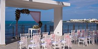 Destination wedding setup on the beachfront at Hotel Riu Cancun, featuring white chairs and a floral arch.