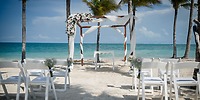 A destination wedding altar with white chairs set up on the sandy beach at Hotel Riu Dunamar by the ocean.