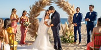 Bride and groom share a kiss at their destination wedding on the beach as guests look on.