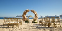 Chairs arranged for a destination wedding face a pampas grass arch on the beach at Hotel Riu Palace.