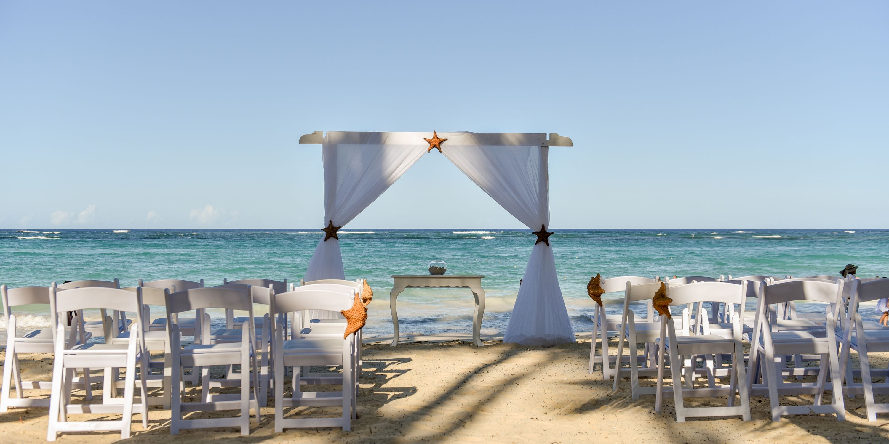 Destination wedding setup at Hotel Riu Palace Bavaro with white chairs and a canopy by the ocean.