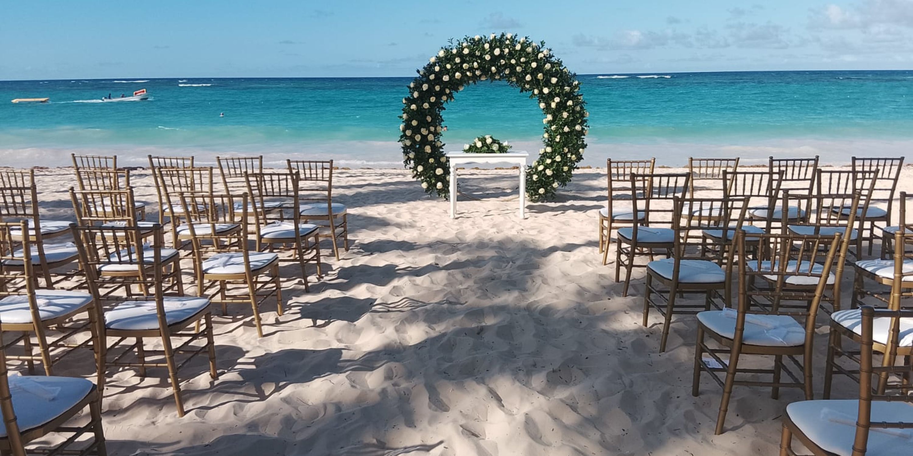 Chairs set for a destination wedding face a floral arch and table on the beach at Hotel Riu Palace Bavaro.