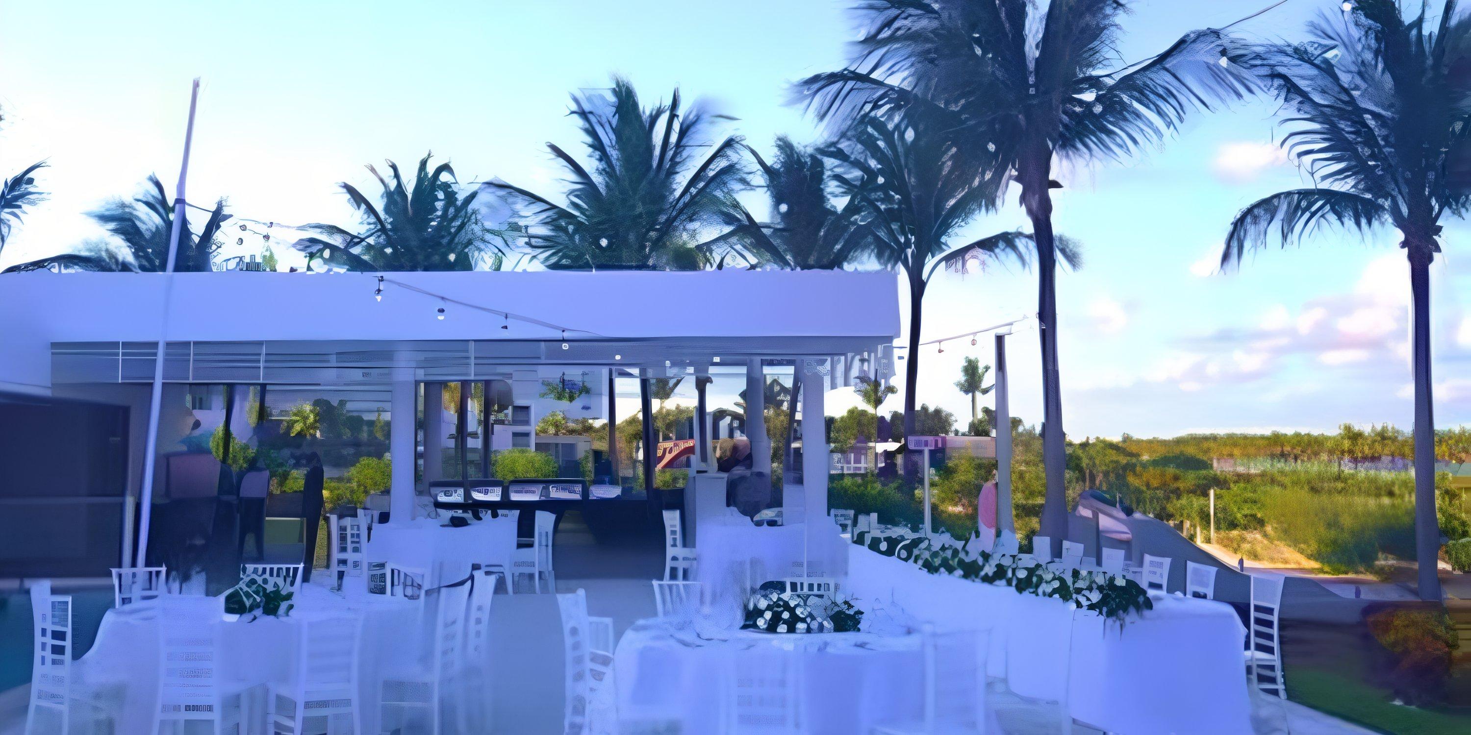 Destination wedding setup with white tables and chairs beneath palm trees at Hotel Riu Palace Costa Mujeres.