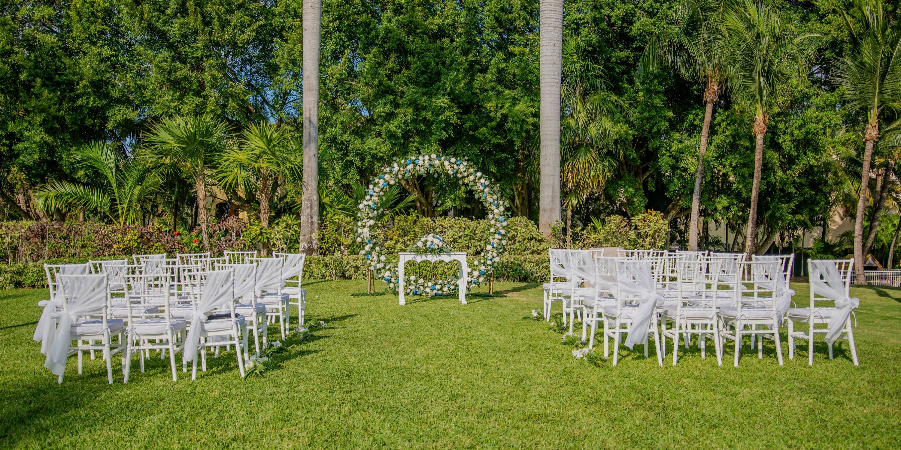 White chairs and a floral arch arranged for a destination wedding ceremony at Hotel Riu Palace Mexico.