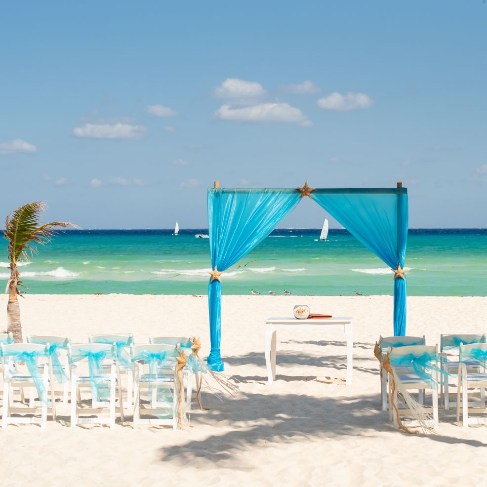 A destination wedding setup featuring blue accents, white chairs, and a scenic ocean backdrop.