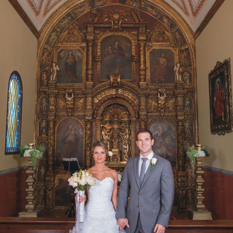 Bride and groom pose for their destination wedding inside a decorated church with an ornate altarpiece.