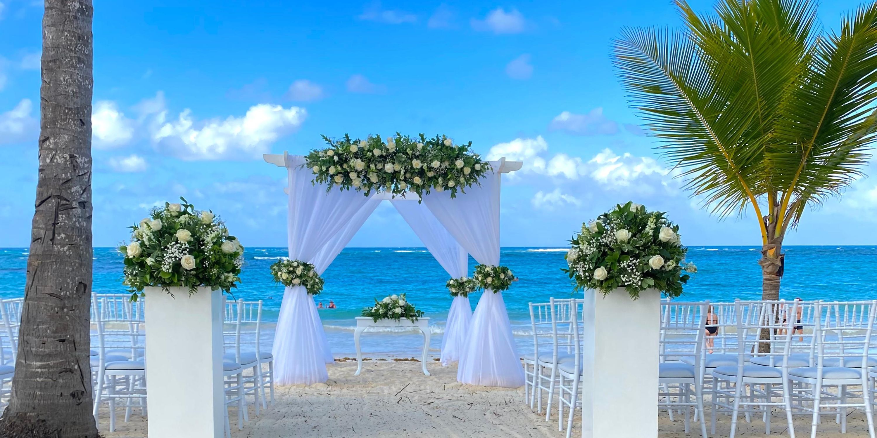 White floral wedding altar at Hotel Riu Palace Punta Cana, chairs arranged for a destination wedding by the ocean.