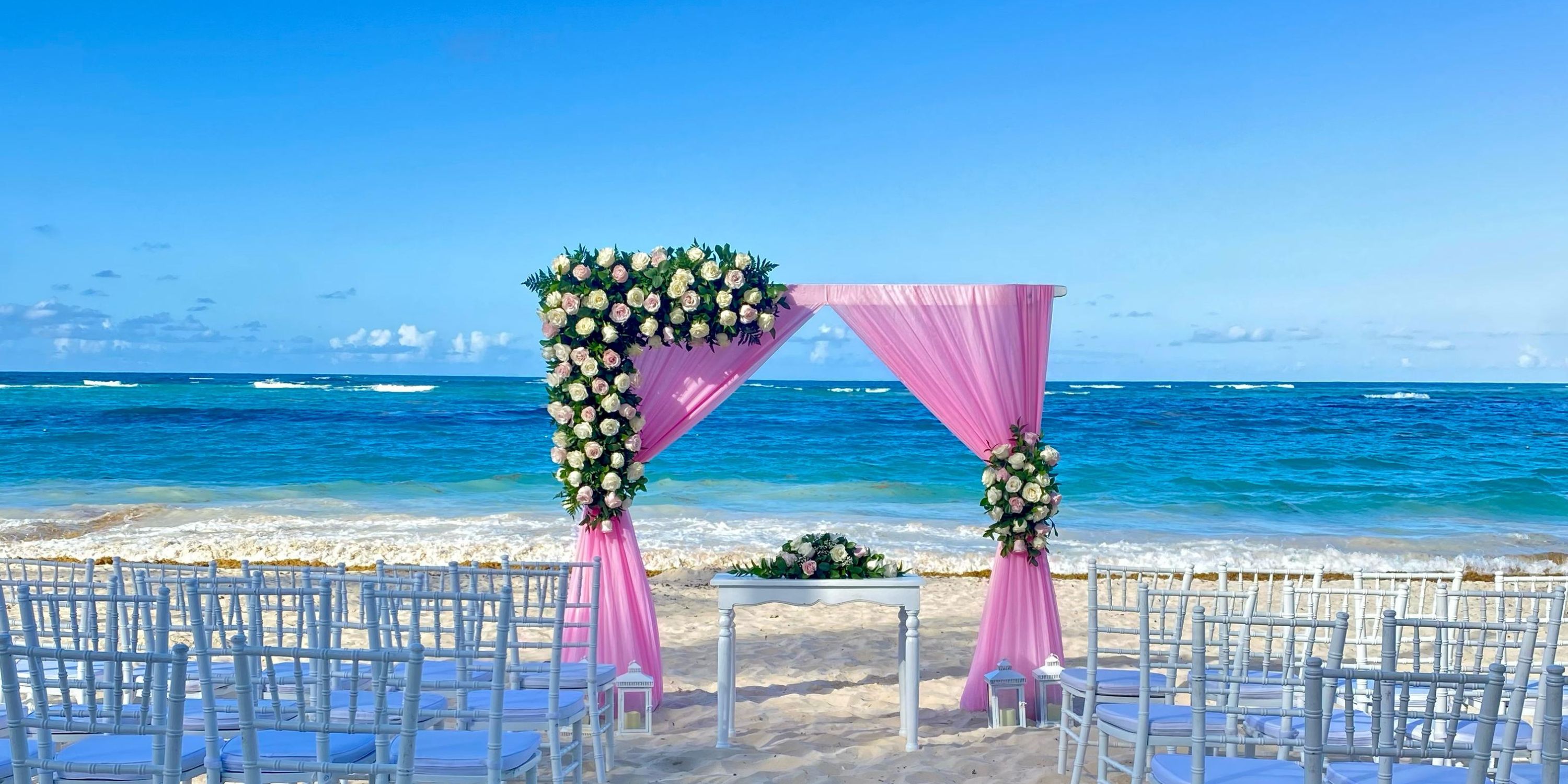 Destination wedding setup at Hotel Riu Palace Punta Cana featuring white chairs and a pink floral arch.