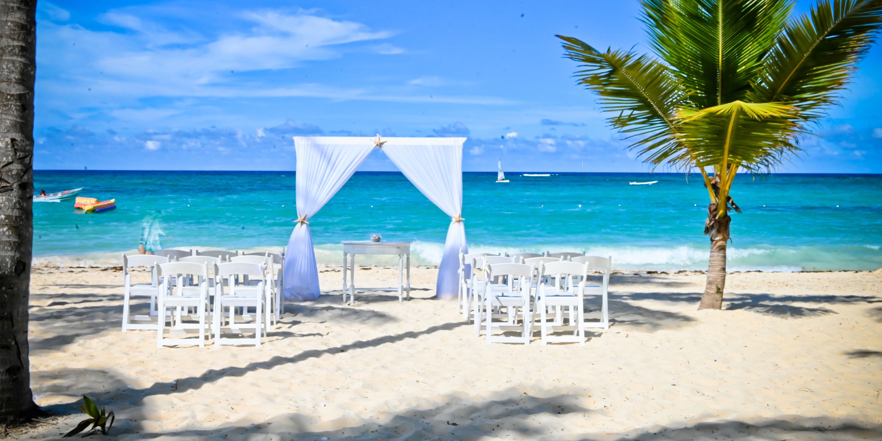 Rows of white chairs face a wedding arch on the sandy beach at Hotel Riu Palace Punta Cana.